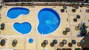 Vista aérea de una zona de piscina con tres piscinas diferentes, rodeada de sombrillas y tumbonas.