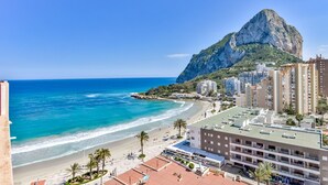 Un hotel frente al mar con vista a la playa y una montaña imponente.