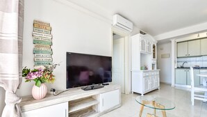 Una sala de estar moderna con un televisor de pantalla plana, una mesa de centro de vidrio y un mueble blanco.