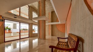 Un hall espacioso con un banco de madera, una entrada con puerta de cristal y suelo de baldosas.