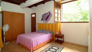 Une chambre à coucher avec un lit, un ventilateur, une armoire, une fenêtre avec des rideaux et un tapis.