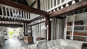 A spacious living room with a large L-shaped sectional sofa, a glass coffee table, and a wooden coffee table. The room features exposed wooden beams, a stone floor, and a bookshelf filled with books. - Full of charm, authentic and renovated cottage Honfleur (Normandy) (Honfleur)