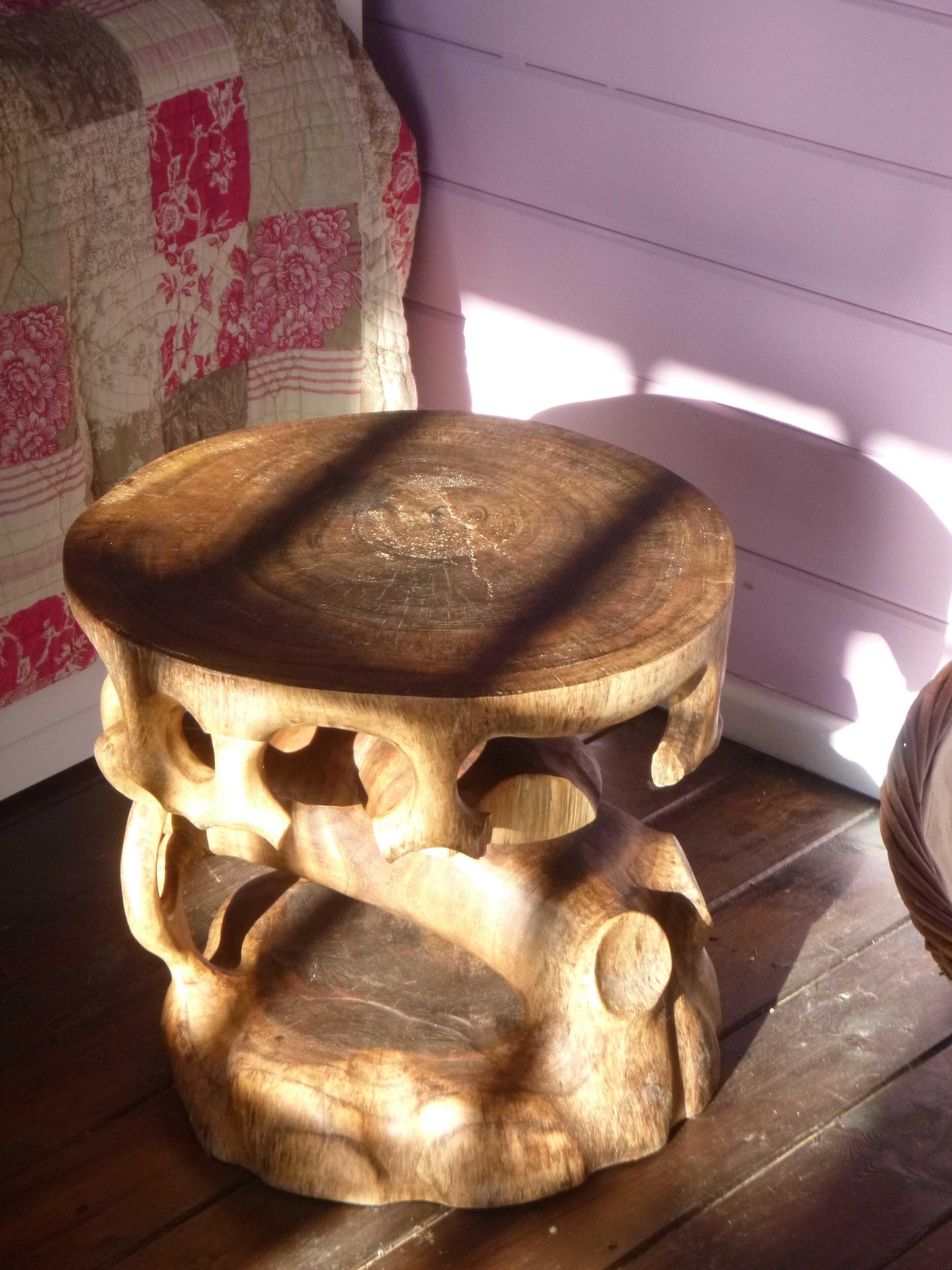 Een houten kruk met een natuurlijke afwerking, geplaatst op een houten vloer.