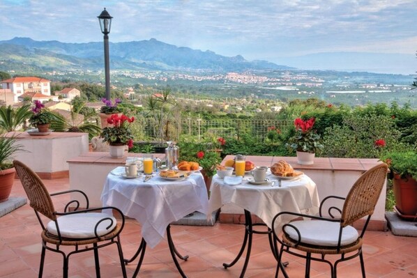 Una terraza con dos mesas dispuestas para el desayuno, con vistas a un paisaje pintoresco que incluye montañas y un pueblo a lo lejos.