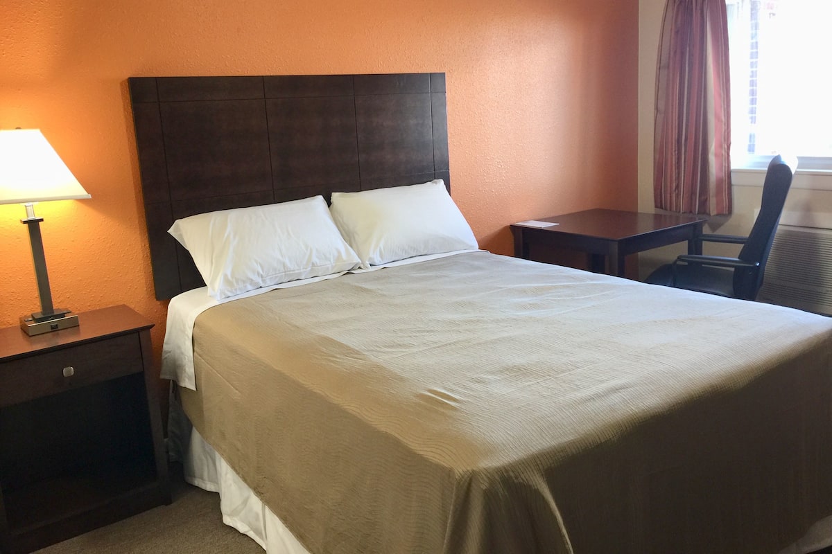 Une chambre d’hôtel avec un grand lit, une table de chevet avec une lampe, une petite table et une chaise.