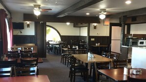 A restaurant with multiple tables and chairs, ceiling fans, and a kitchen area. - Downtown Motel (Woodward)