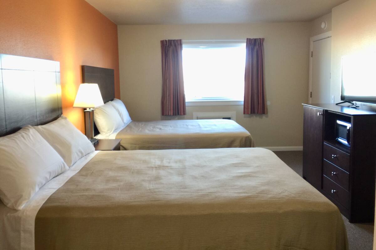 Une chambre d’hôtel avec deux lits, un bureau avec une lampe, une commode et un téléviseur.