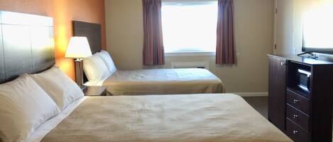 A hotel room with two beds, a desk with a lamp, a dresser, and a television.