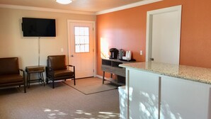 A compact living space with a kitchenette, a flat-screen TV mounted on the wall, a seating area with two chairs, and a door with a window. - Downtown Motel (Woodward)