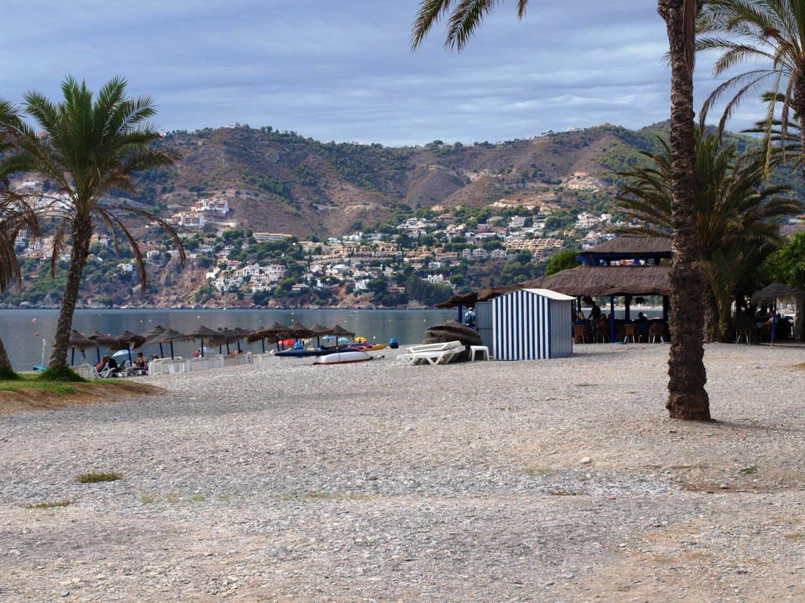 Una playa con un edificio pequeño, palmeras y barcos.