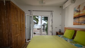 Een slaapkamer met een bed, een houten garderobe en uitzicht op het strand.
