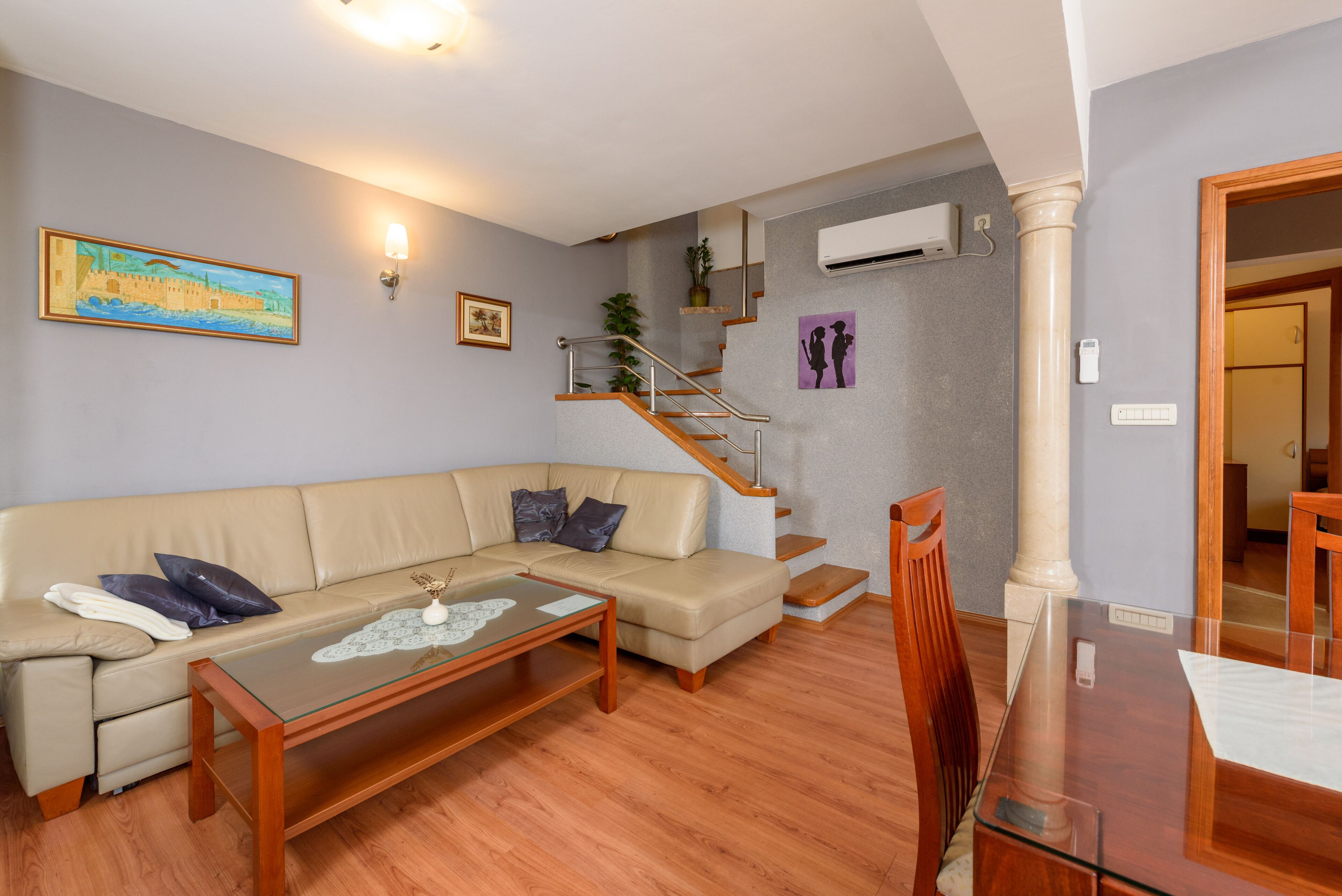 A living room with a beige sofa, a glass coffee table, and a wooden dining table.