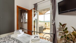 Een slaapkamer met een bed, een televisie, een balkon met een stoel en een plant.