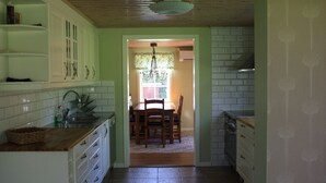 A kitchen with white cabinets, a wooden countertop, and a tiled backsplash. There is a dining area with a table and chairs visible through an open doorway.