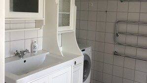 A modern bathroom with a white vanity, a built-in washing machine, and a towel rack.