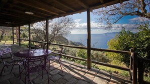 Ein überdachter Außenbereich mit Tisch und Stühlen, mit Blick auf eine malerische Landschaft mit Bäumen und dem Meer.