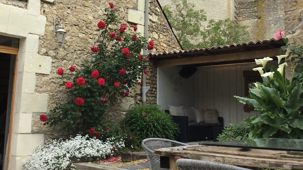 Une cour avec un bâtiment en pierre, une tour ronde et une table entourée de chaises.