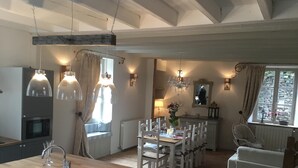 Une cuisine moderne avec un plan de travail en bois, des armoires blanches et un four encastré. On y trouve également un coin repas avec des chaises blanches et une table dressée pour deux personnes.