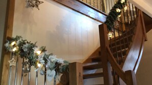 Un escalier en bois avec une rampe, décoré de guirlandes et d’ornements de Noël.