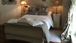 Une chambre avec un mur en pierre, un lit avec des oreillers, une table de chevet avec une lampe et un miroir.