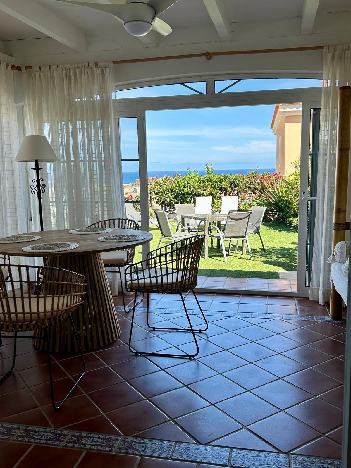 Ein Essbereich mit Tisch und Stühlen, einem Deckenventilator und Blick auf das Meer durch große Glasüren.