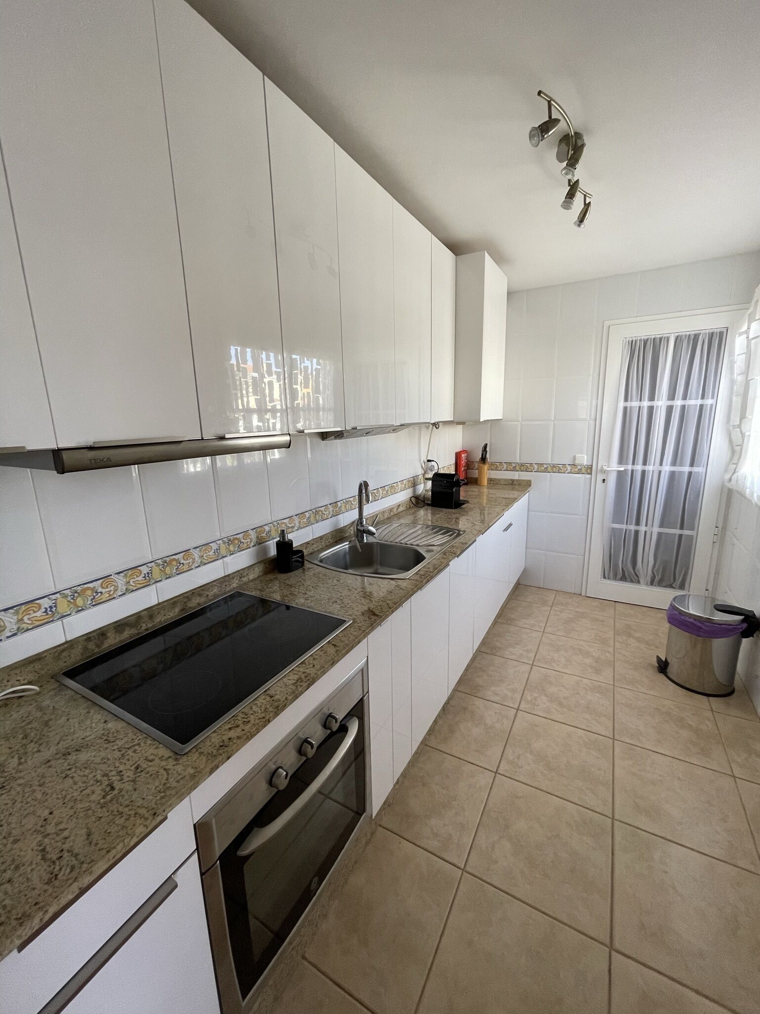 Una cocina con gabinetes blancos, un lavamanos doble, una estufa y un cubo de basura.