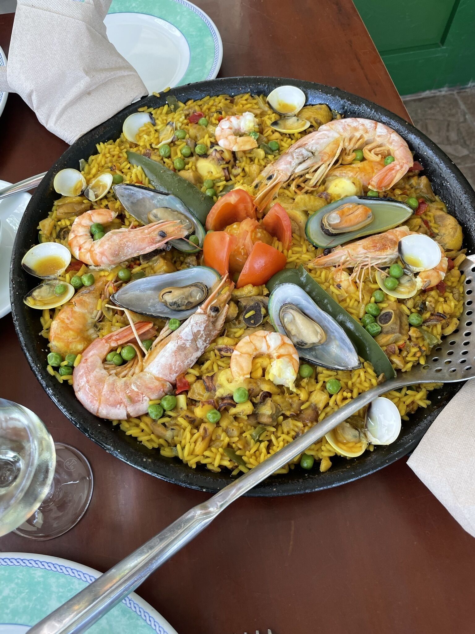 Une grande paella aux fruits de mer est servie sur une table, accompagnée d’une fourchette et d’une cuillère.