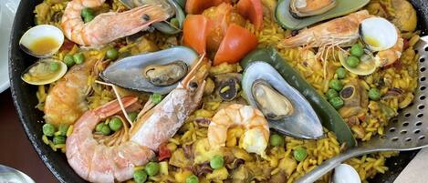 Une grande paella aux fruits de mer est servie sur une table, accompagnée d’une fourchette et d’une cuillère.