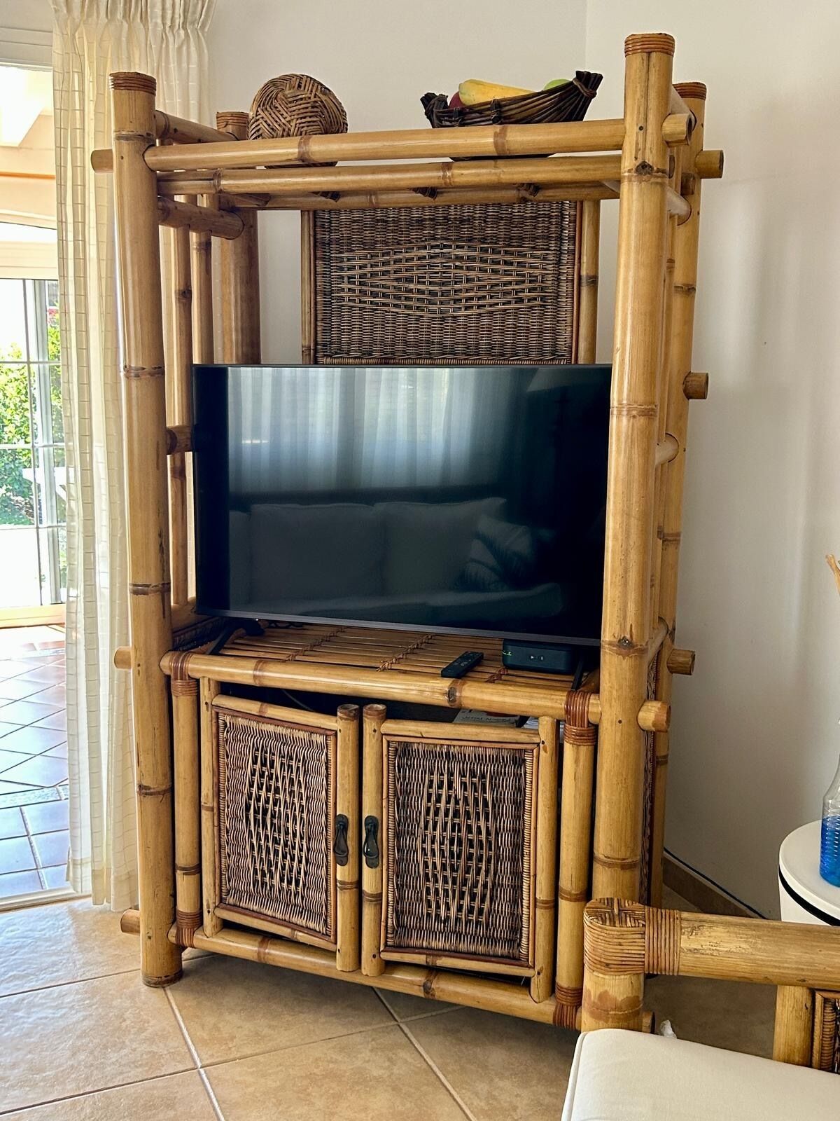 Un mueble de entretenimiento con estructura de bambú, televisor de pantalla plana, espacios de almacenamiento de mimbre y un control remoto encima.