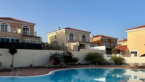 Une piscine dotée d’une terrasse carrelée, entourée d’immeubles avec des balcons, sous un ciel bleu dégagé.