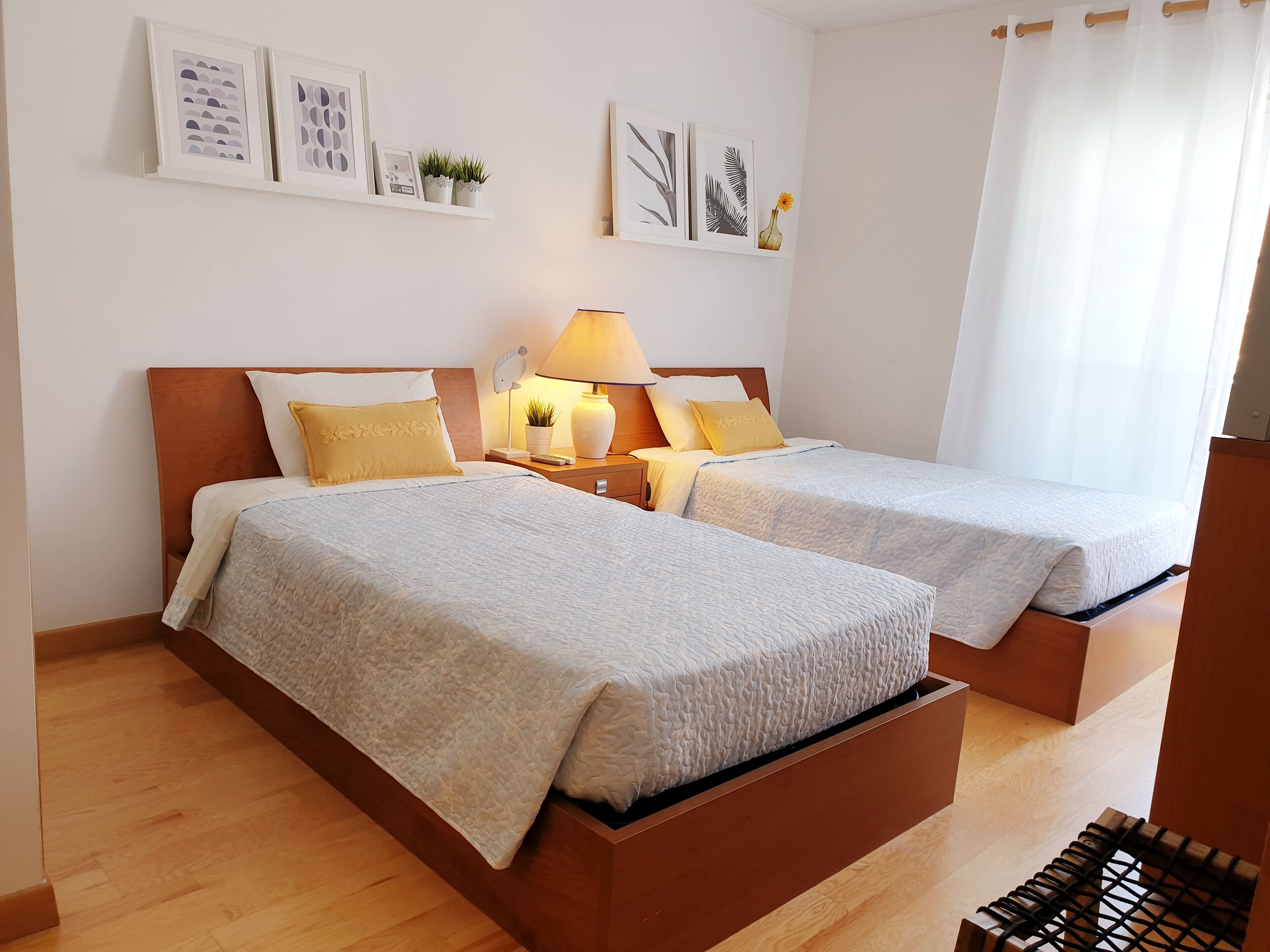 Une chambre d’hôtel avec deux lits, une table de chevet avec une lampe, une petite plante et des œuvres d’art encadrées au mur.