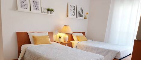 Une chambre d’hôtel avec deux lits, une table de chevet avec une lampe, une petite plante et des œuvres d’art encadrées au mur.