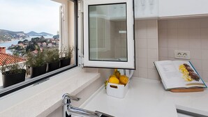 Una cucina con vista su una cittadina costiera, un lavello con una pianta in vaso e un libro sul bancone.