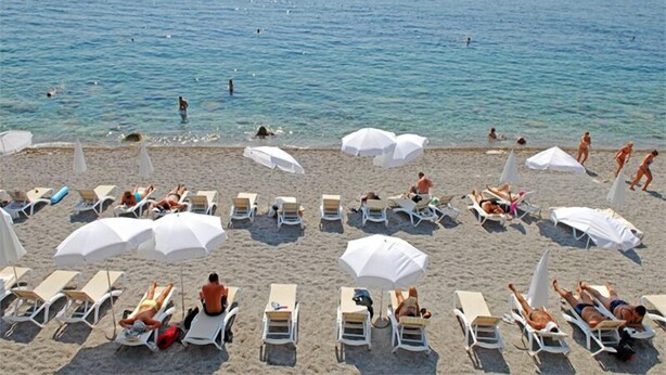 Una spiaggia con file di lettini e ombrelloni, alcuni dei quali occupati da persone.