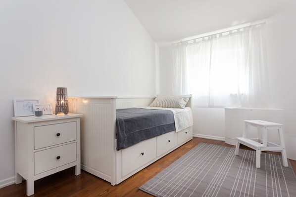 Een slaapkamer met een bed, nachtkastje en een witte bijzettafel.