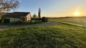 A rural landscape with a house, a field, and a sunset.