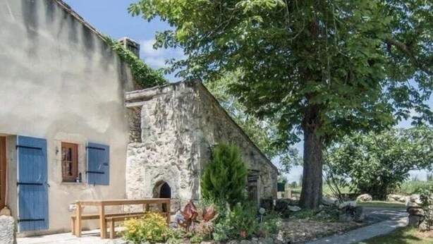 A rustic stone building with a wooden bench and a small garden area.