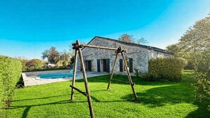 A stone building with a swimming pool, a swing set, and a well-maintained lawn.