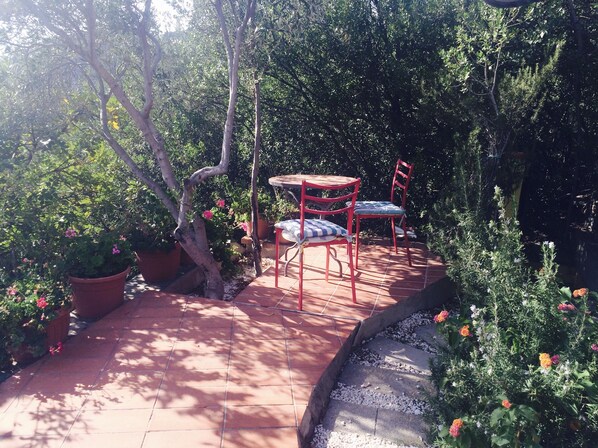A patio with a tiled floor, surrounded by potted plants and a small table with chairs.