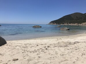 Une plage à l’eau d’un bleu limpide, bordée d’un rivage sablonneux et ponctuée de formations rocheuses.