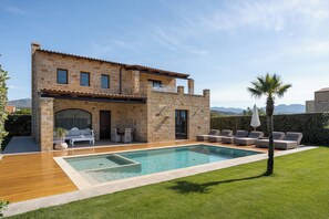 Une maison en pierre à deux étages, dotée d’une piscine, d’un espace salon extérieur et offrant une vue sur les montagnes.