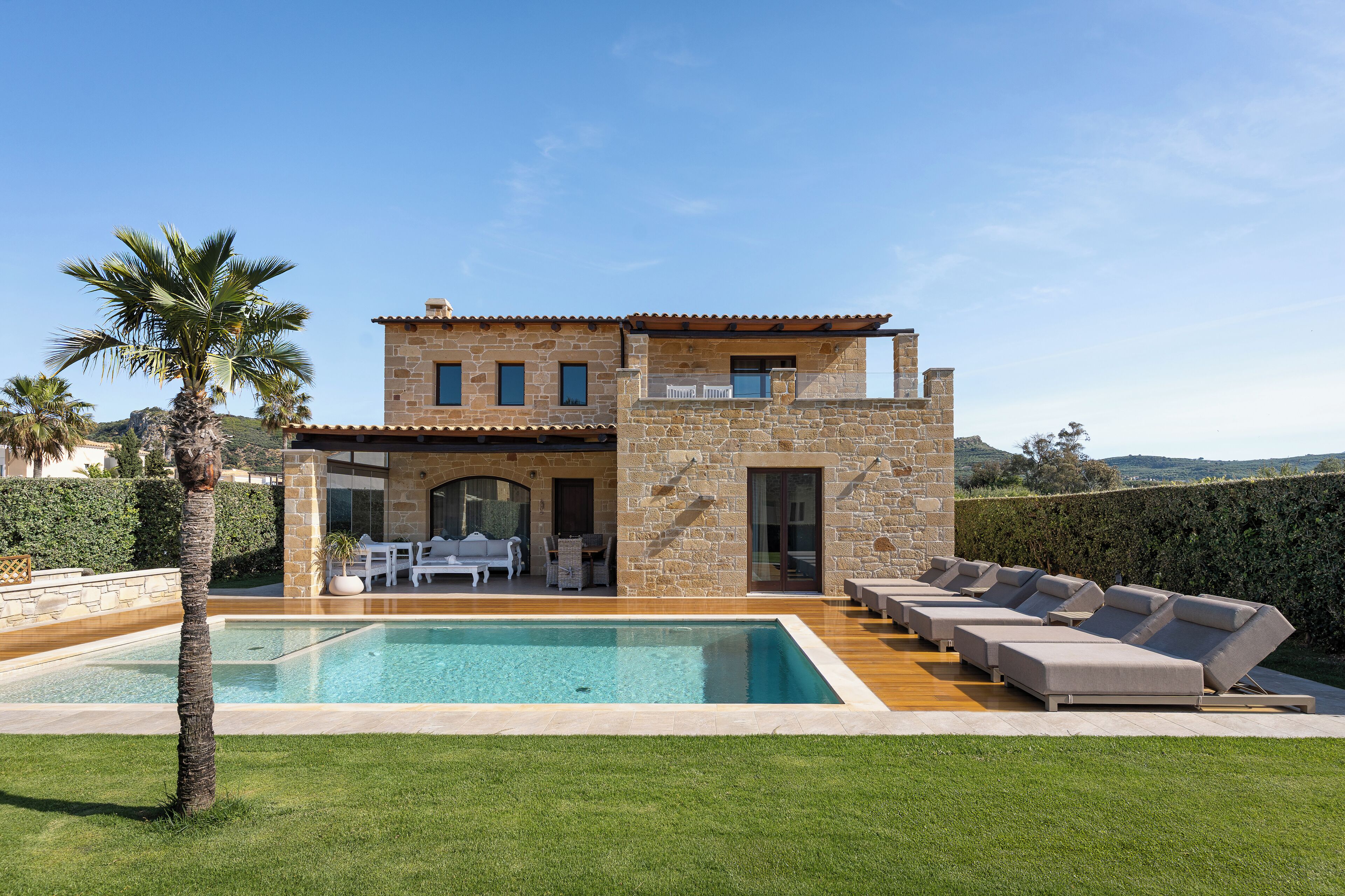 A two-story stone house with a swimming pool, outdoor seating, and a view of the countryside.