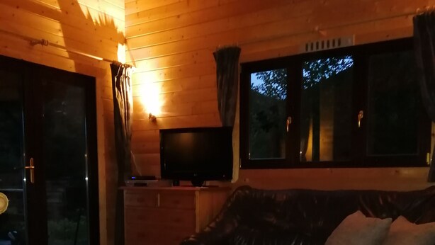 A cozy living room with a wooden ceiling, a black leather sofa, a white coffee table, and a television on a wooden stand.