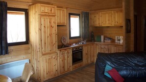 A wooden cabin interior with a kitchen area, a dining table, and a black leather sofa.