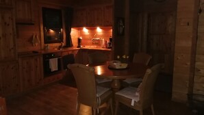 A cozy wooden cabin interior with a dining area, a kitchen with wooden cabinets, and a clock on the wall.