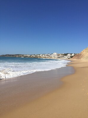 A beach with a clear blue sky, sandy shore, and a distant cityscape.