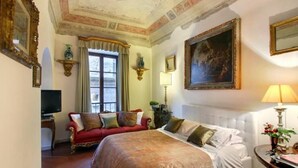 A hotel room with a large bed, a red sofa, a television, and a painting on the wall. - Luxury Apartment in Florence "TERRAZZA DE' MEDICI" (Firenze)