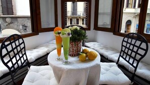 A corner seating area with white cushioned chairs and a small round table. The table has a white tablecloth and is adorned with a potted plant and a fruit arrangement. - Luxury Apartment in Florence "TERRAZZA DE' MEDICI" (Firenze)