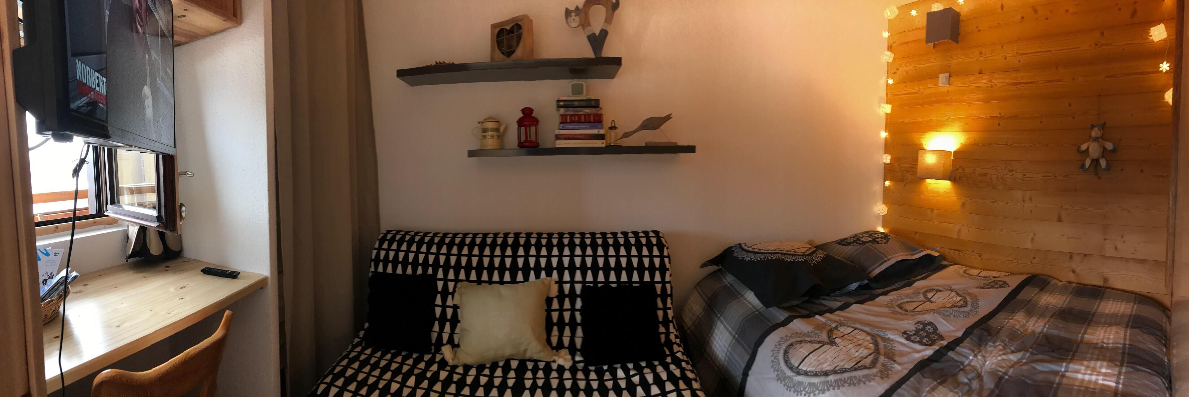 A cozy room with a bed, a desk with a computer, and shelves with books and decorative items.