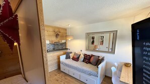 Ein kompakter Wohnraum mit einer Küchenzeile, einem Sofa mit vielen Kissen, einem kleinen Tisch und einem Fernseher.